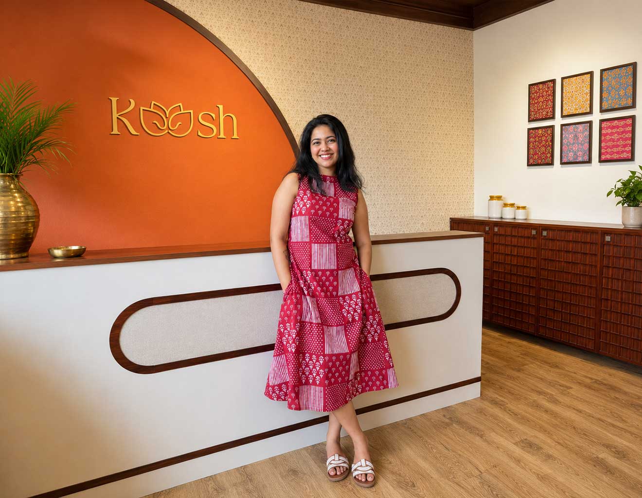 Woman in a red dress standing in front of a reception desk with 'Koosh' branding.